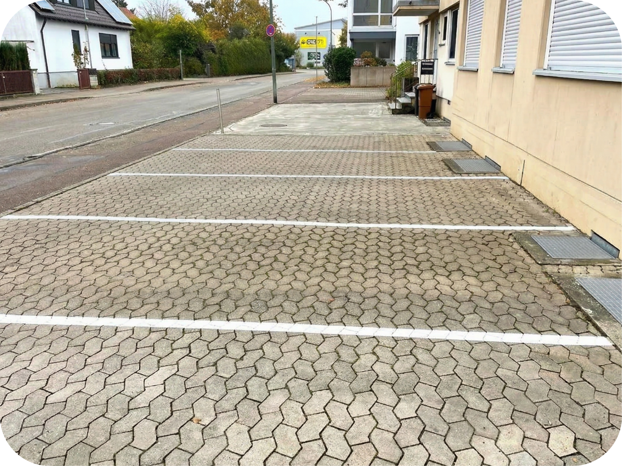 Ein leerer Parkplatz mit sauberen, hellgrauen Verbundpflastersteinen. Fünf saubere, weiß gestrichene Parklinien sind aufgebracht.