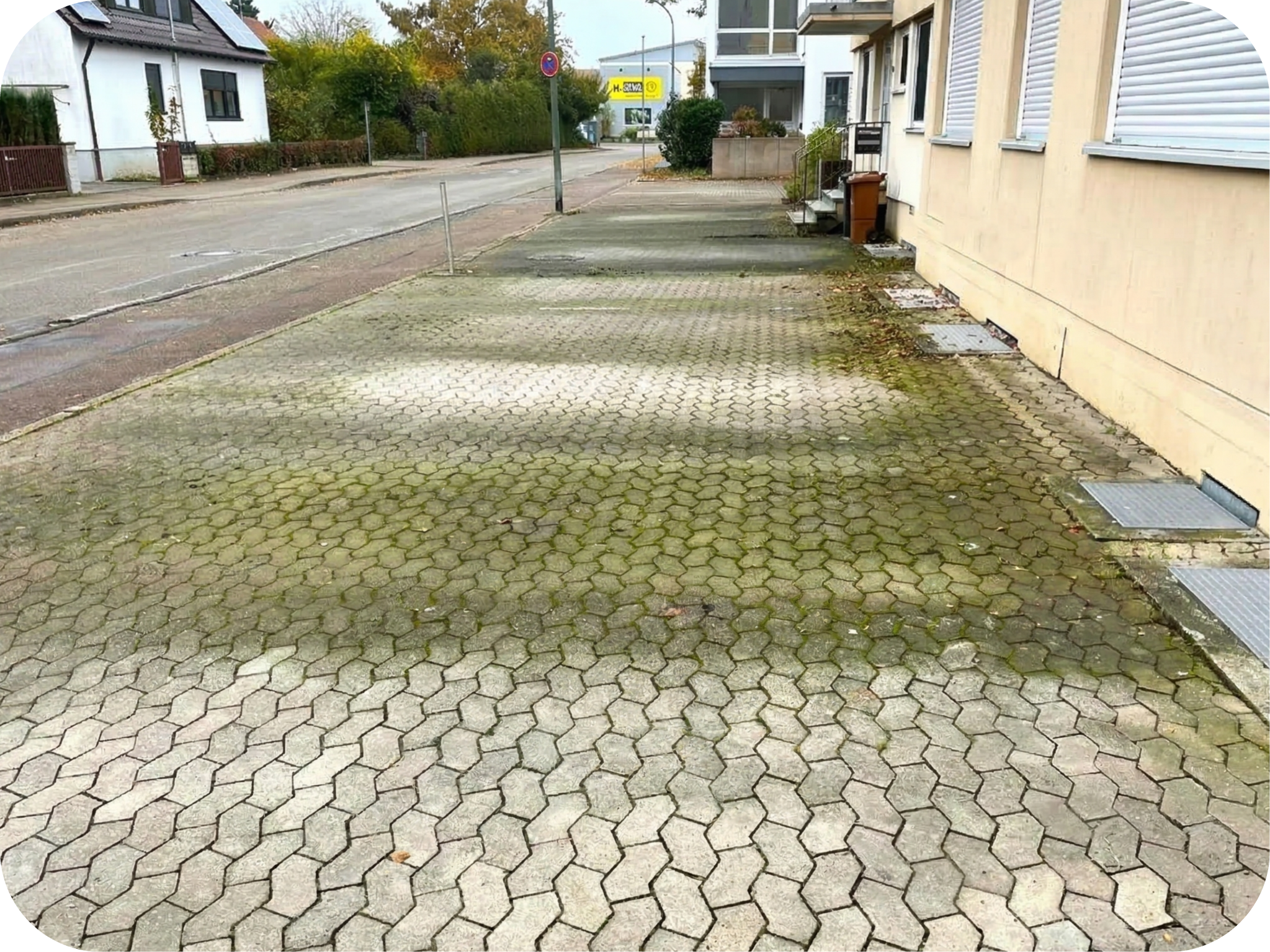 Ein leerer Parkplatz mit stark veralgten und moosigen Verbundpflastersteinen. Die Hauswand und der Hintergrund sind sauber und statisch.